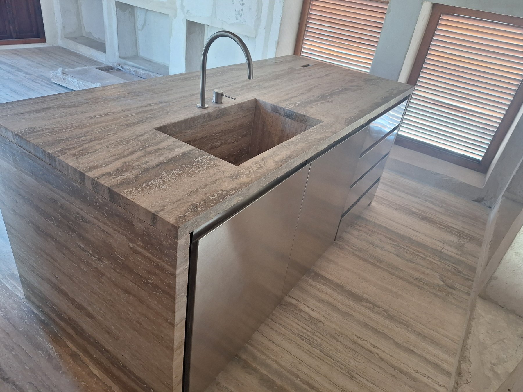 Stainless steel cabinet doors and drawers on a travertine kitchen island with integrated sink