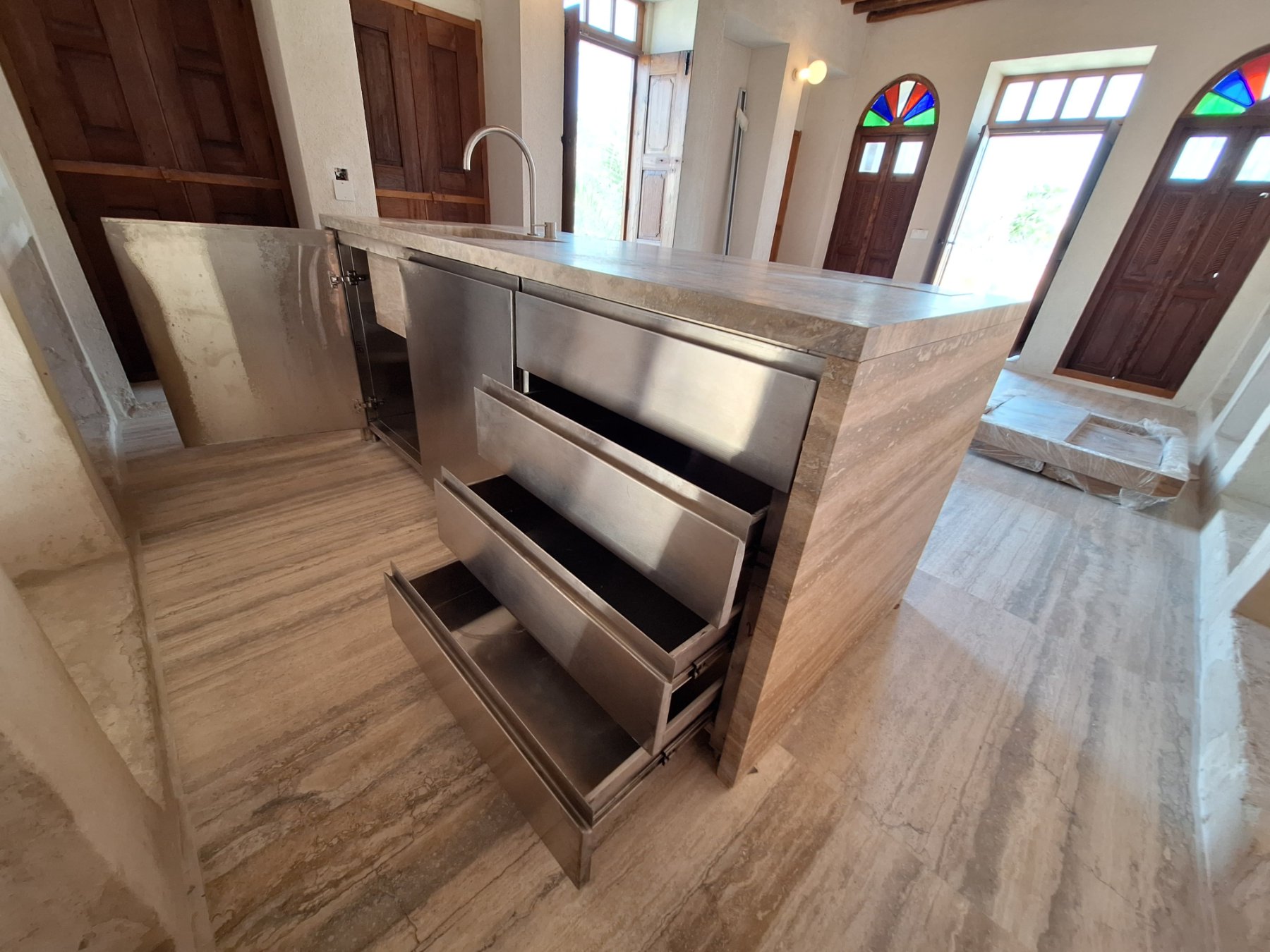 Open stainless steel drawers and cabinet door of a travertine-clad kitchen island