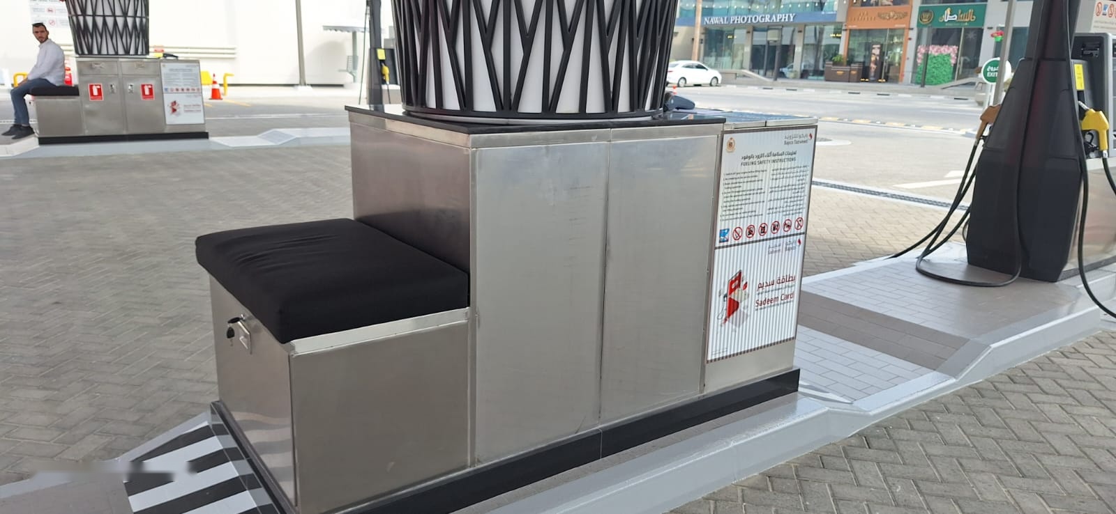 Stainless steel fuelling-island cabinet with seat and safety instructions panel beside a pump