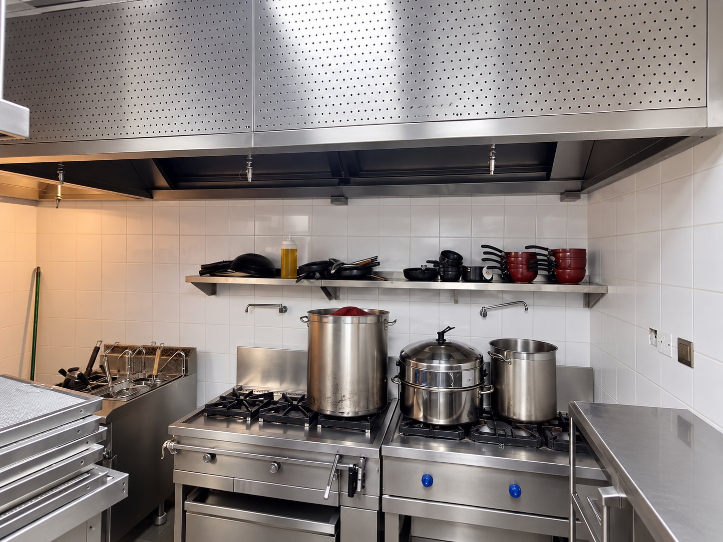 Cooking ranges under a perforated stainless steel canopy with a shelf of pans