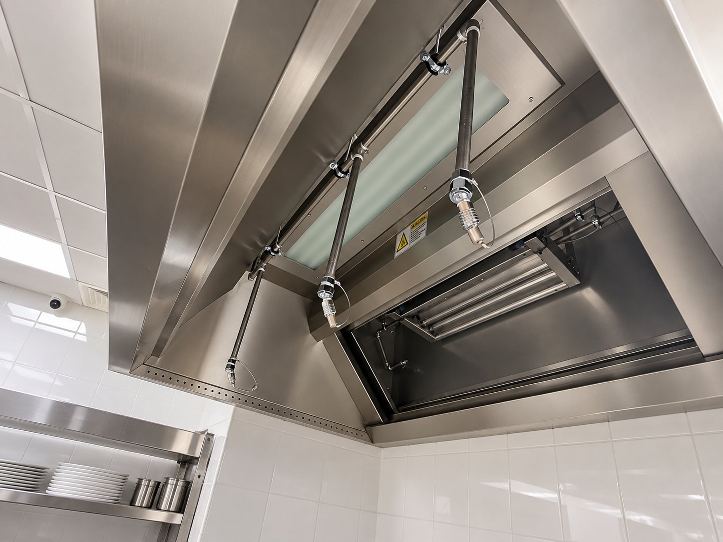 Underside of a stainless steel extraction canopy with fire-suppression nozzles and lighting