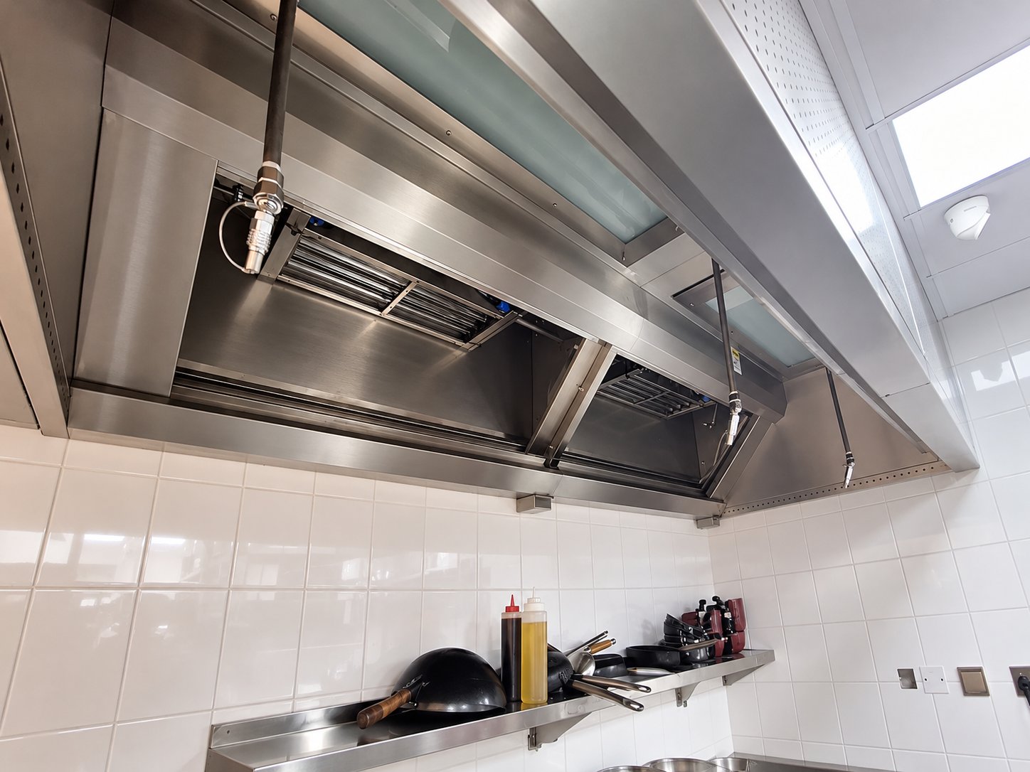 Stainless steel kitchen canopy with grease filters, fire-suppression pipework and wall shelf