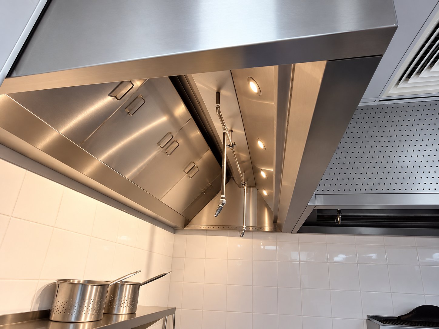 Extraction canopy with recessed lights and fire-suppression nozzles above a stainless steel work table