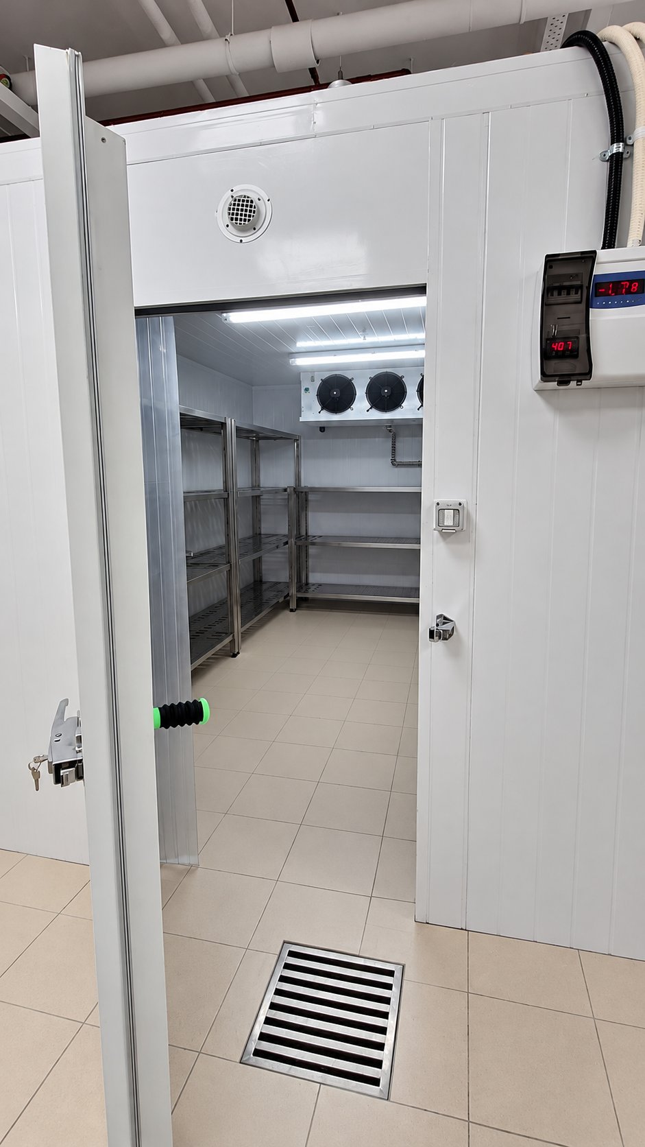 Open door of a walk-in cold room with stainless steel shelving and digital temperature controller